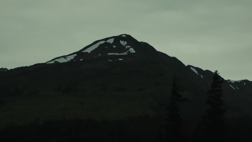Mountain covered with vegetation and patches of snow under a cloudy sky