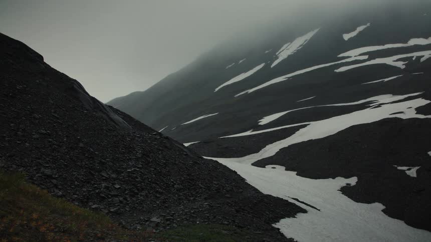 Steep rocky mountains with patches of snow under foggy sky