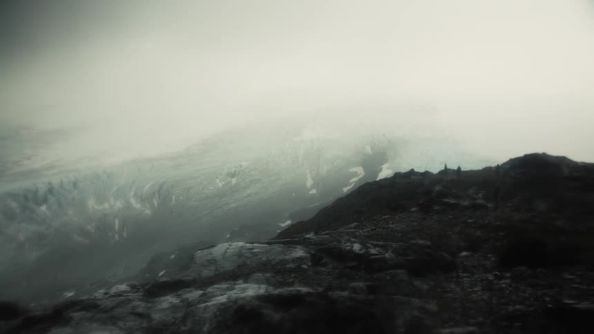 Desolate rocky landscape with dense fog rugged terrain and glacier in the background under overcast sky