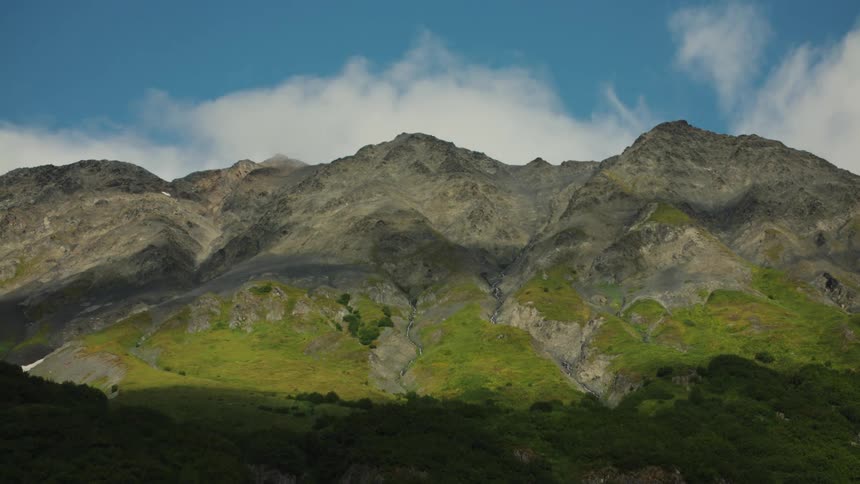 A mountain range with rugged terrain stretches under the bright midday sun