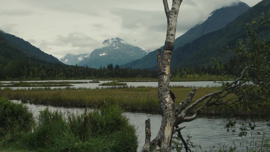 A creek winds through a mountainous region bordered by grassland under a cloudy sky