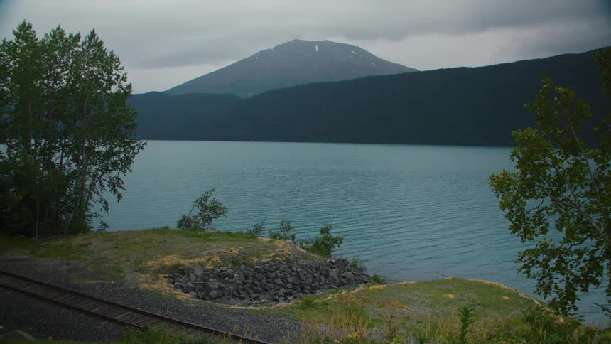 Lake with hills and a mountain to one side and a train rail to the other outdoors during day time