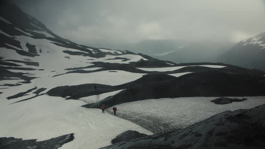 People walking across a snowcovered mountainous terrain under a cloudy sky
