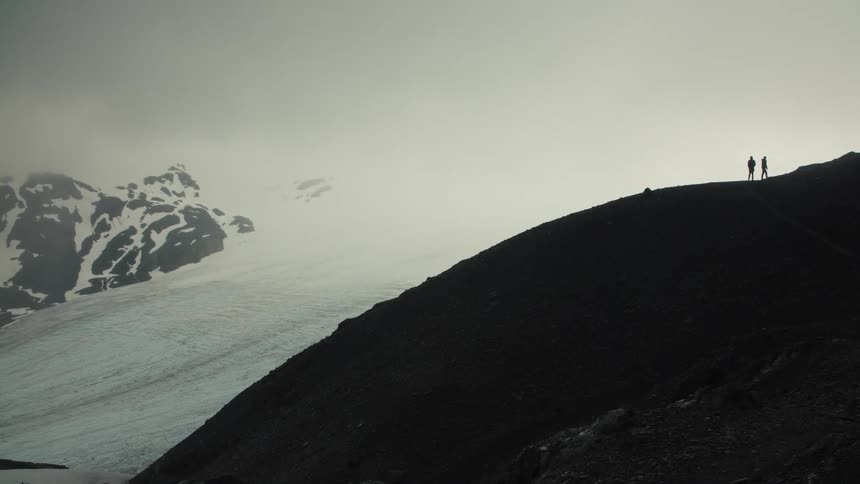 Small group of hikers walking around a slope next to ice and snow outdoors