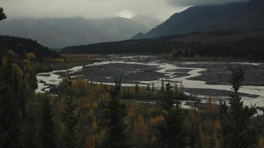 Winding river flowing through a valley surrounded by forests and mountains under a cloudy sky