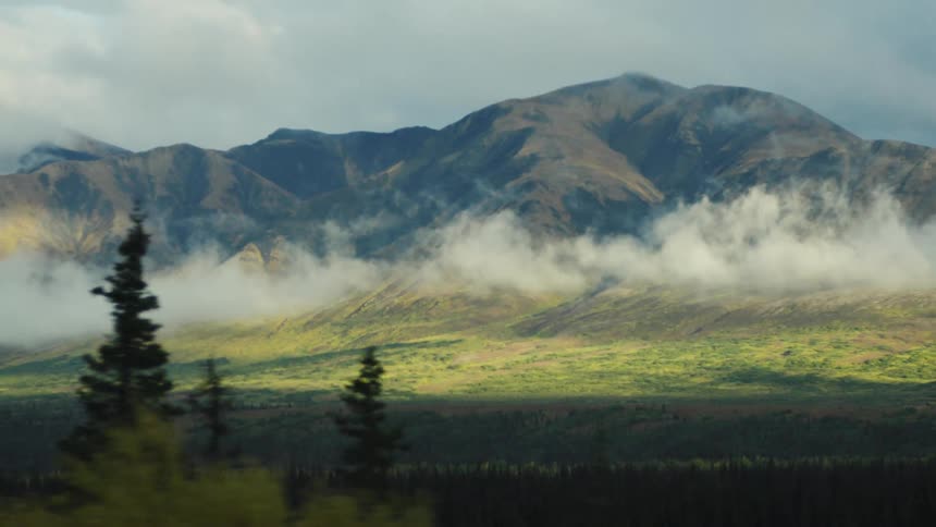 Majestic mountains with low clouds over a lush green plain
