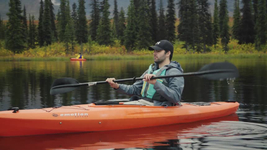 A young man paddling an orange kayak on a river during daytime