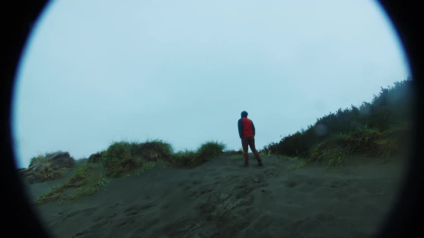 A man walks up a hill on a cloudy day dressed in a sweatshirt