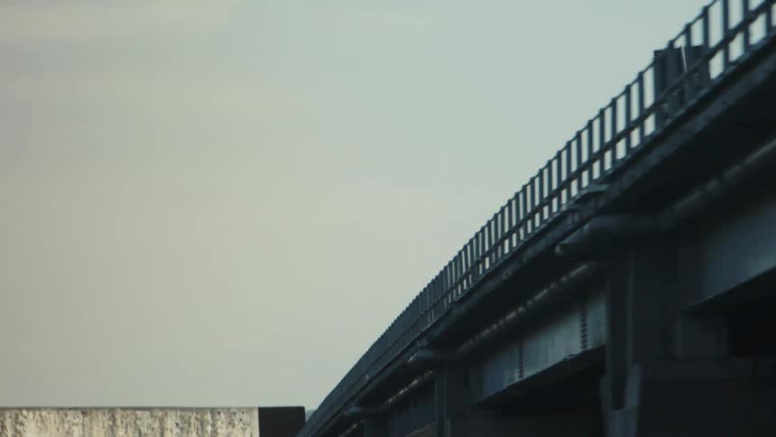 A long bridge extends toward distant hills under a clear sky