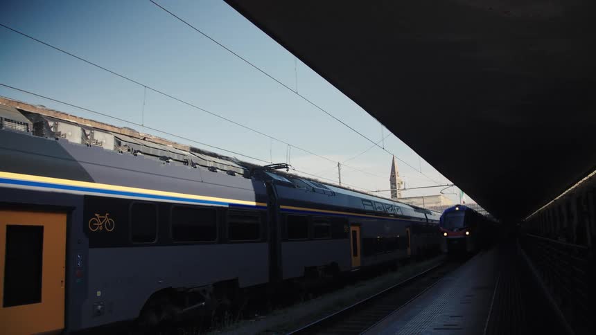A train pulls into a station at midday its cars gliding along the tracks beneath the bright sun