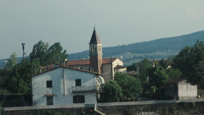Old church building surrounded by houses and trees with hills and natural landscape on the background outdoors during day time