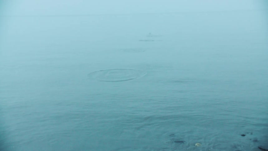 Small rock emerges on the calm sea surface under a cloudy sky