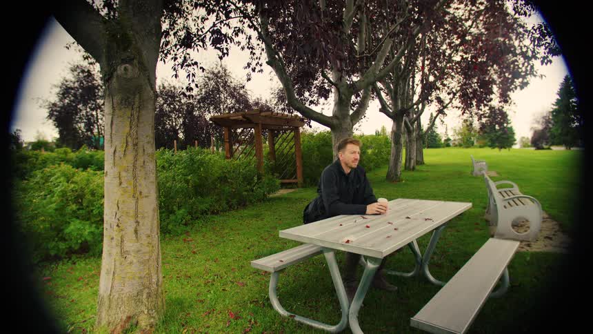 Man sitting at picnic table and drinking in wooded park