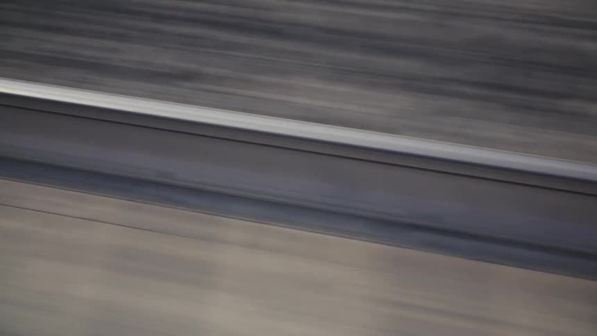 A vehicle speeds along the road at midday with the asphalt surface and lane separator clearly visible