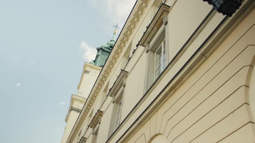 The sunlit facade of a historic building where a green topped steeple with a cross rises against the bright sky