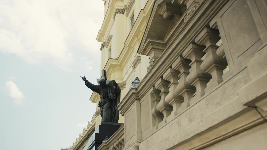 Statue with a raised cross atop the ornate balcony of a historic building