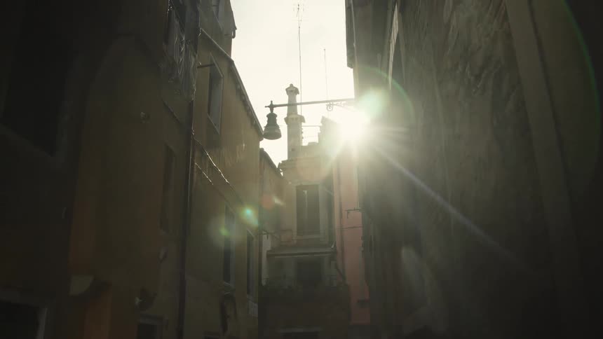 Sunlight streams through a narrow alley between old buildings at sunset