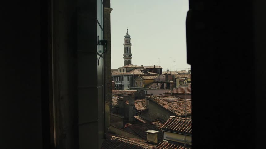 A scenic view of old european rooftops and a bell tower framed through a window