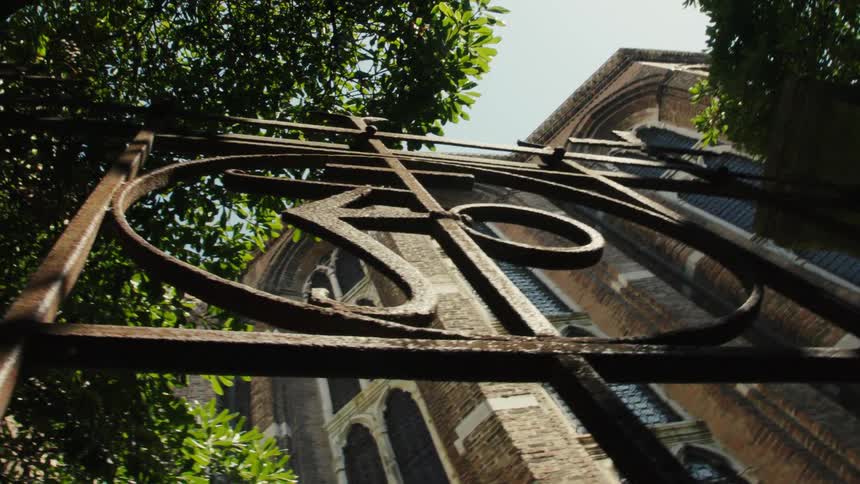 Ironwork containing an abstract symbol stands near a historic building on a summer day