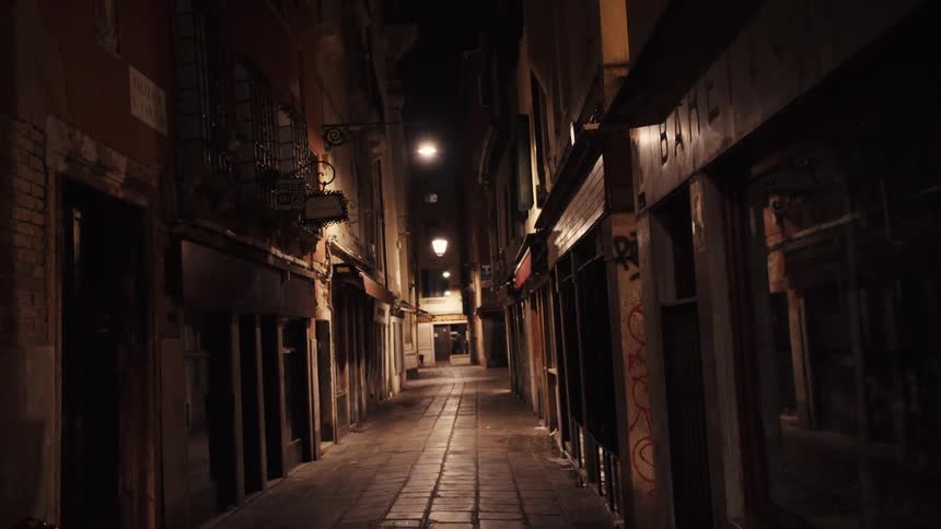 Shops line a narrow paver covered street at night