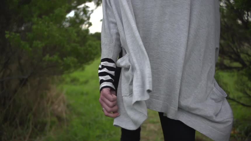 A person is walking on a grassy path, while the back of their jackets swings to and fro