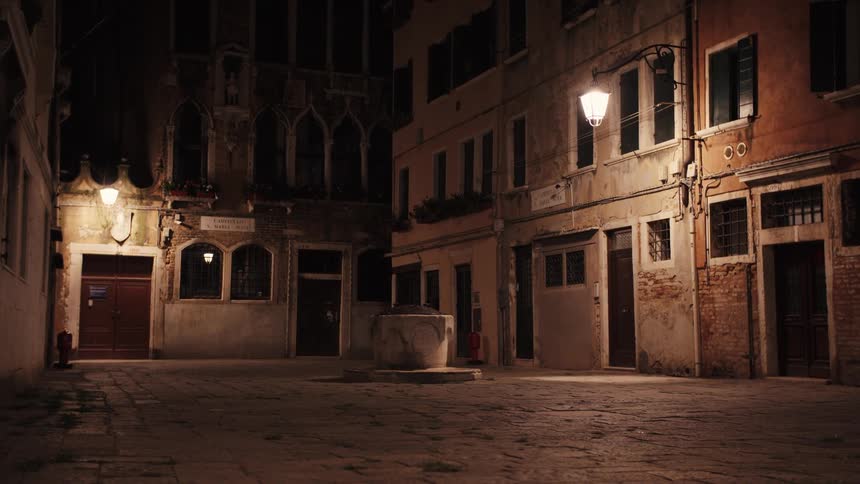 A stone courtyard with old buildings lit by a few street lamps at night