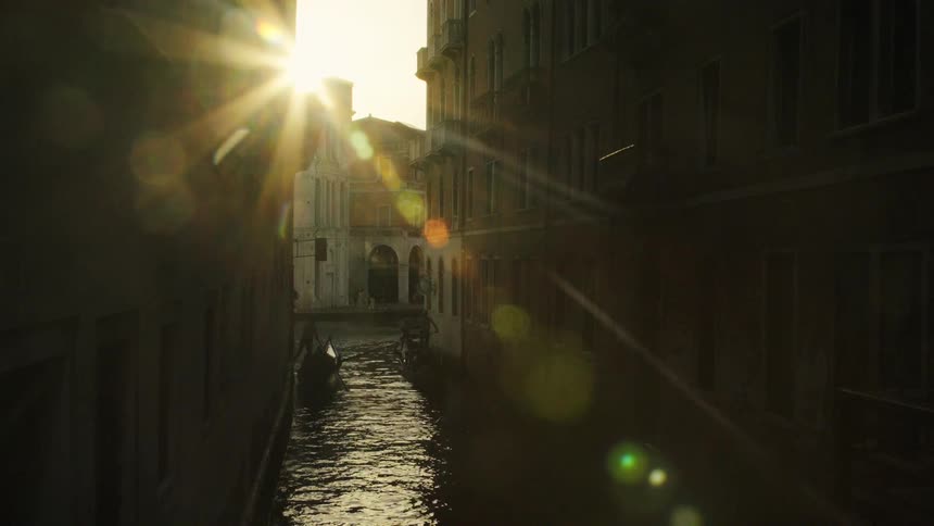 Narrow canal between buildings with boat on the water and low sun lighting the scene
