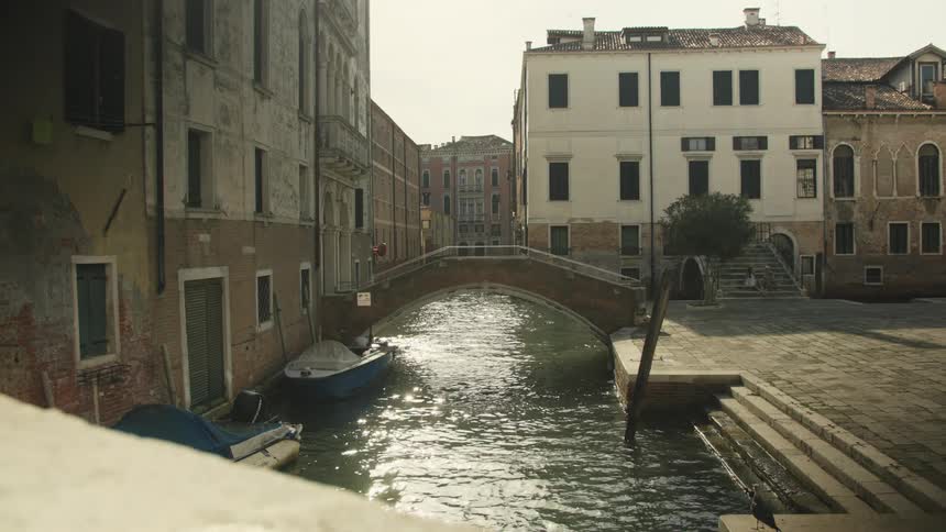 A city at midday with a canal running through it a bridge spanning the water and a boat docked beside a building