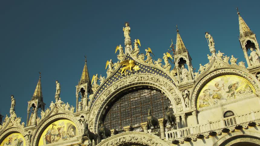 The video is an extreme lowangle shot of the highly ornamented facade of an ornate cathedral almost certainly st marks basilica in venice with the sky as the backdropthe focus is on the row of five arches featuring intricate gold mosaics