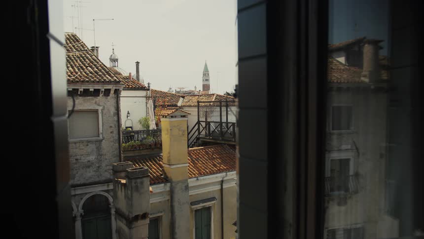 Framed by the window jambs a sunlit view stretches over weathered venetian rooftops and terraces to a distant campanile