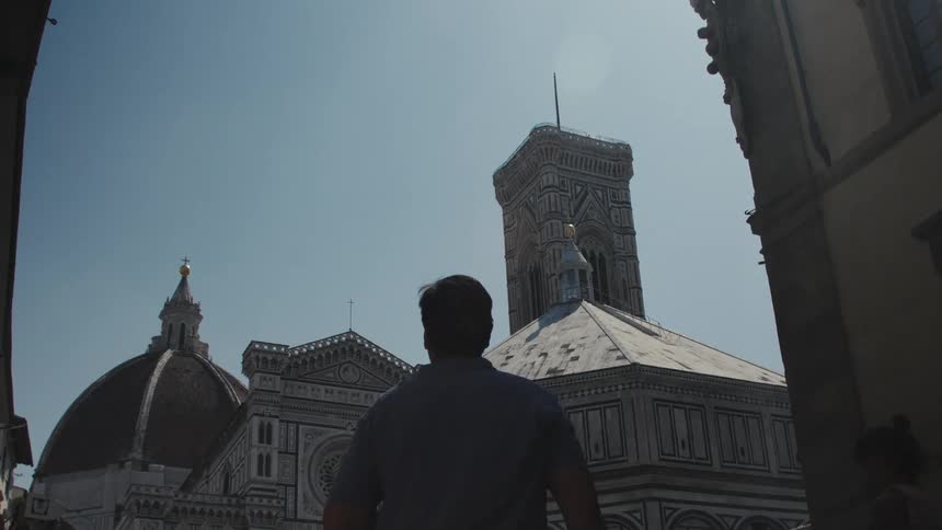 A man stands in shadow in florences piazza del duomo gazing up at the cathedral dome and giottos bell tower