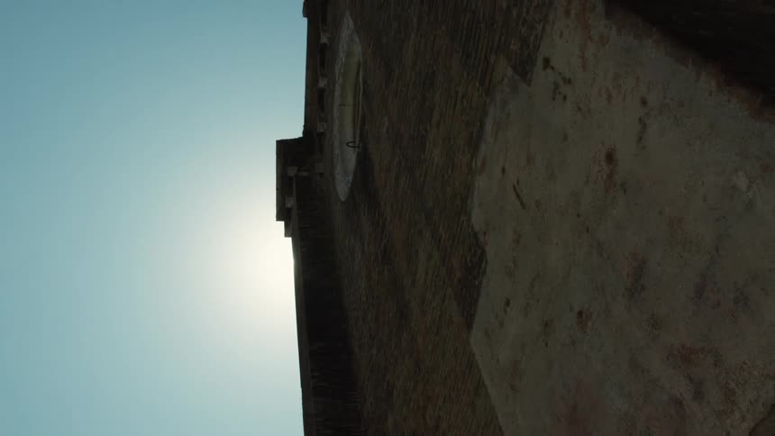 Brick structure viewed from below with circular opening at the top and sunlight creating silhouette