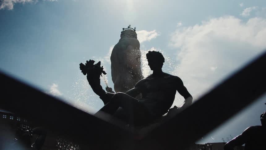 A fountain with a statue silhouetted against the sky on a sunny day