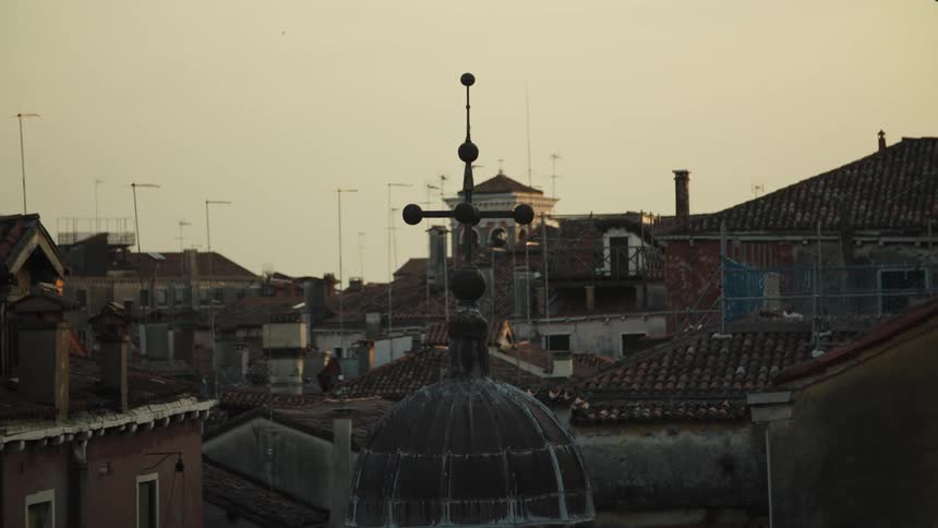 At golden hour a small dome topped by a cross of stacked spheres rises amid terracotta rooftops and tv antennas