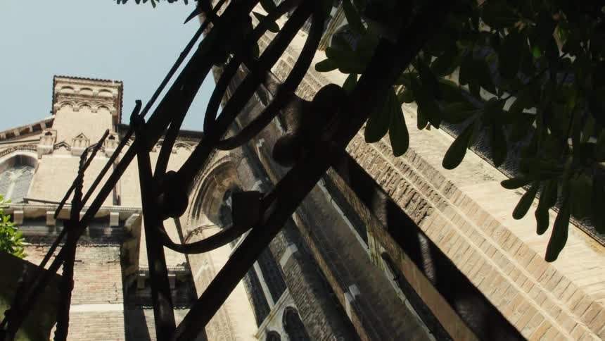 Facade of a historic brick building seen from below through an iron gate