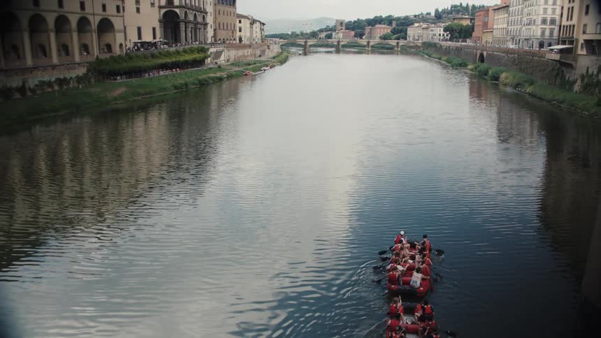 Two rowboats full of people travel up the canal in the city