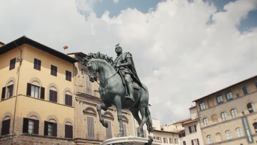 The video shows a closeup of a large bronze equestrian statue set against a backdrop of historical buildings under a slightly cloudy sky the statue depicting a man in armor on horseback appears to be located in a european city square
