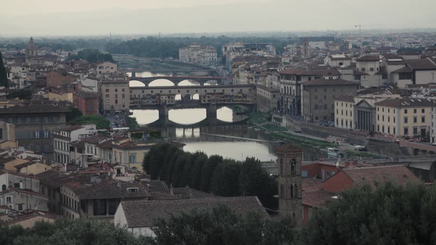 Ponte vecchio reflected in the arno river surrounded by terracottaroofed buildings and surrounding greenery