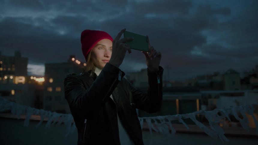 Woman wearing a red beanie holding a phone to take a photo at dusk