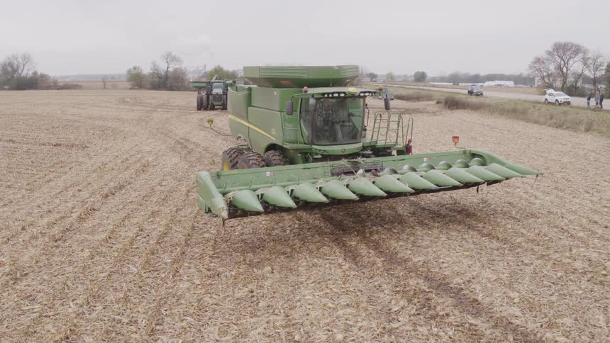 Agricultural machine moves across a field while people standing on the highway watch on an autumn day