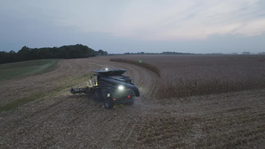 Harvester operating at dusk in a vast crop field