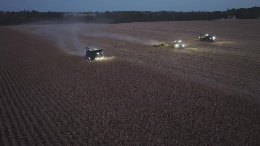 Illuminated agricultural machines working on a nighttime harvest in a large field