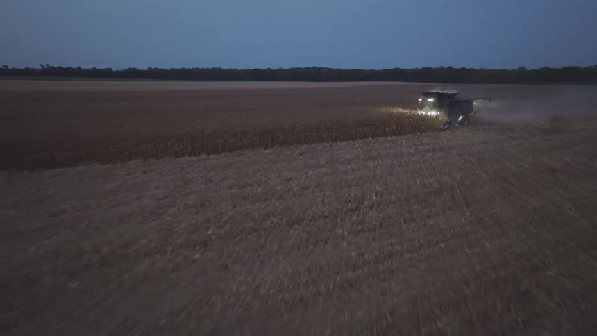 The video is a lowangle aerial shot taken during the harvesting of a field at night the frame is dominated by the bright powerful headlights of two tractors or combines kicking up clouds of dust as they work in the dark