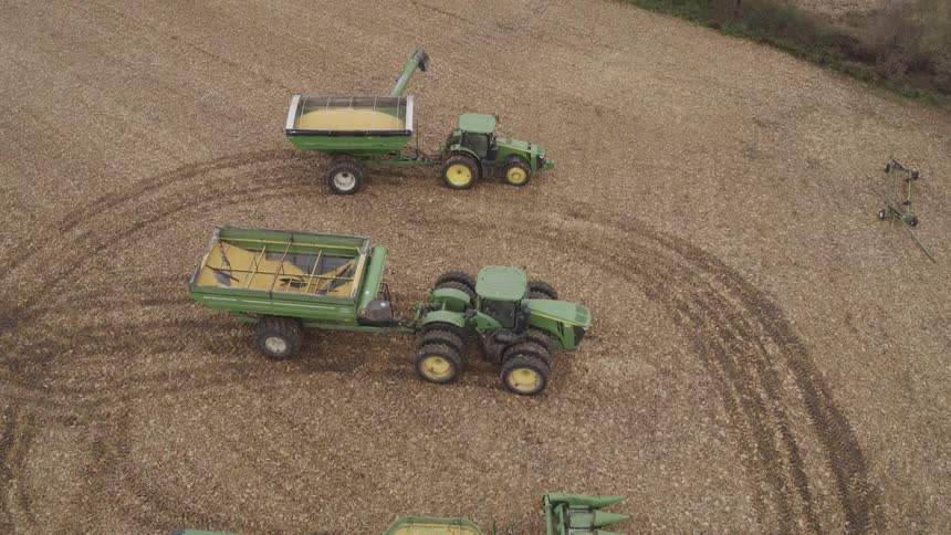 Combine harvesters lined up in an agricultural field with tire marks on the ground