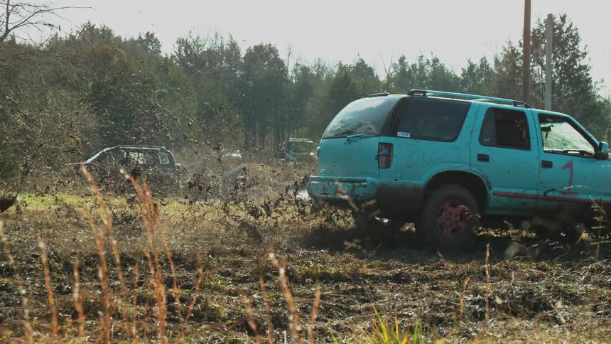 Blue suv covered in mud driving through an offroad terrain in a rural area