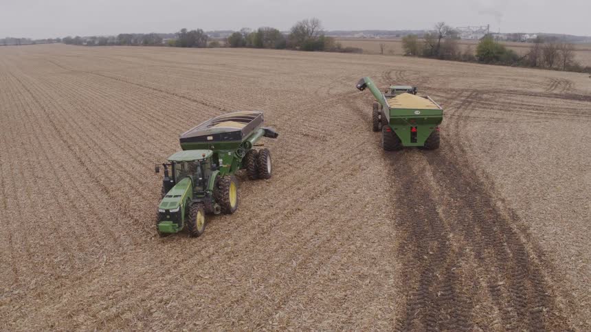 Tractors and a combine harvester operating in a vast field during harvest