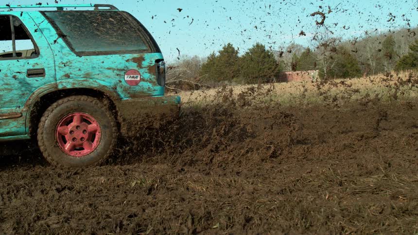 Blue mudcovered car speeding on a muddy terrain