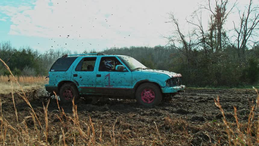 Blue suv covered in mud driving through a muddy outdoor area