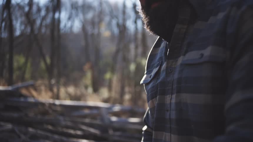 Close up of a man cleaning the blades of a chainsaw while standing outdoors in a woodland during daytime