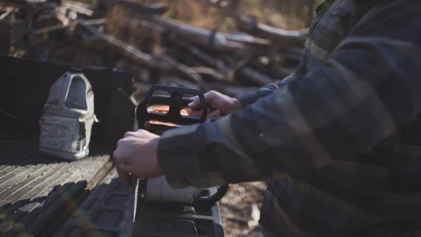 Person handling a chainsaw on the bed of a vehicle in a logged forest area